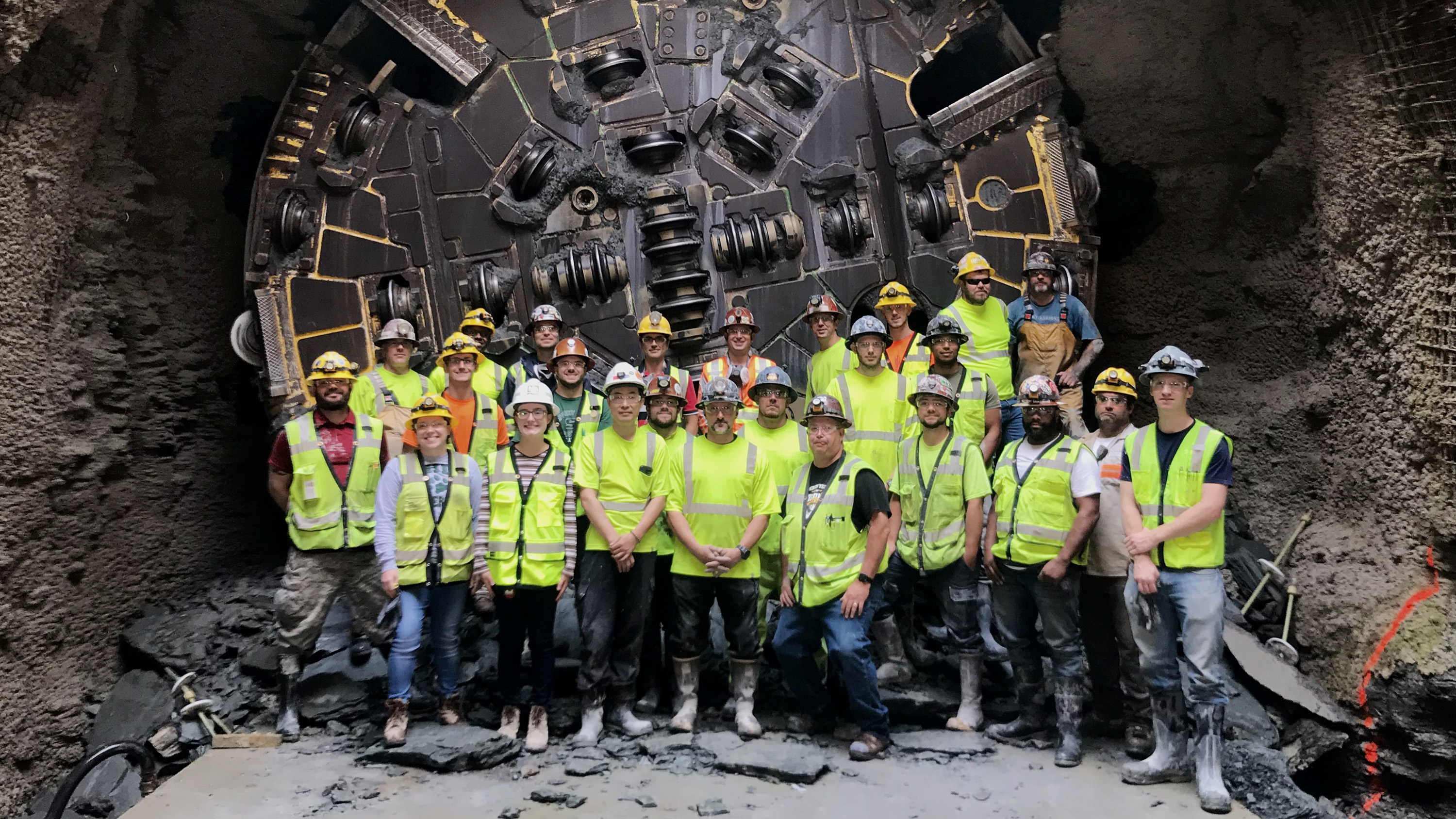 Tunnel construction workers standing in front of a tunnel boring machine that broke through.